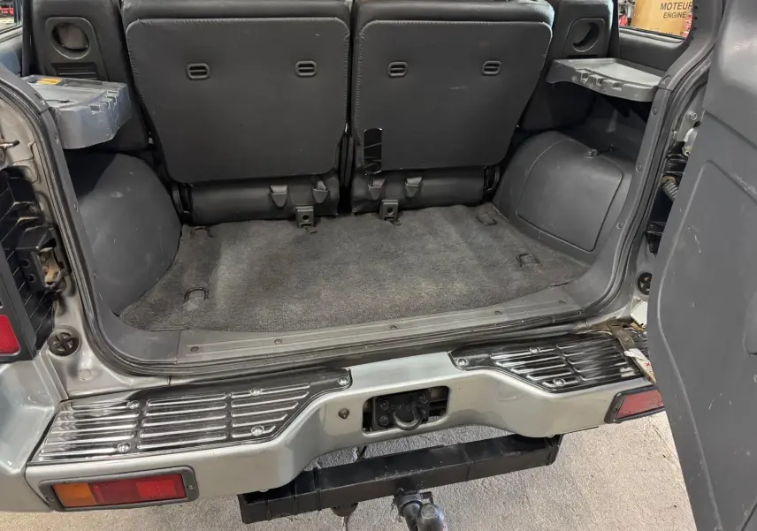 Vue arrière ouverte du Mitsubishi Pajero Court gris aluminium de 1997, montrant l'espace de coffre et l'attelage.