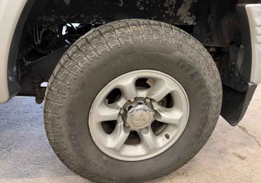 Gros plan sur la roue avant droite gris aluminium du Mitsubishi Pajero Court 2.8 TD avec jante alliage et logo central visible.