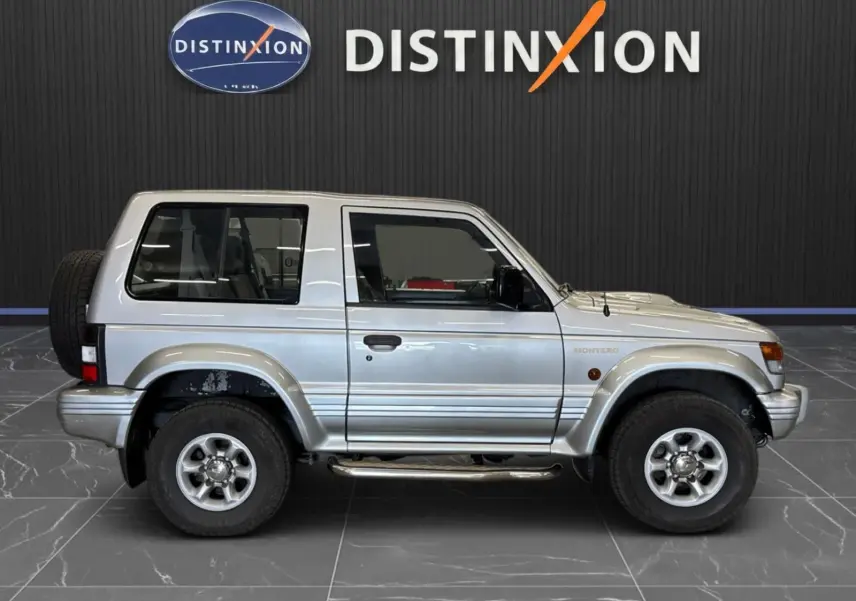 Profil droit du Mitsubishi Pajero Court gris aluminium de 1997 avec marchepieds et jantes alliage 15 pouces.