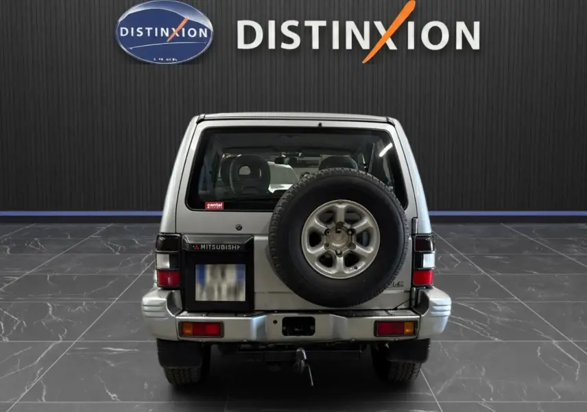 Vue arrière d'un Mitsubishi Pajero Court gris aluminium de 1997 avec roue de secours et attelage visible.