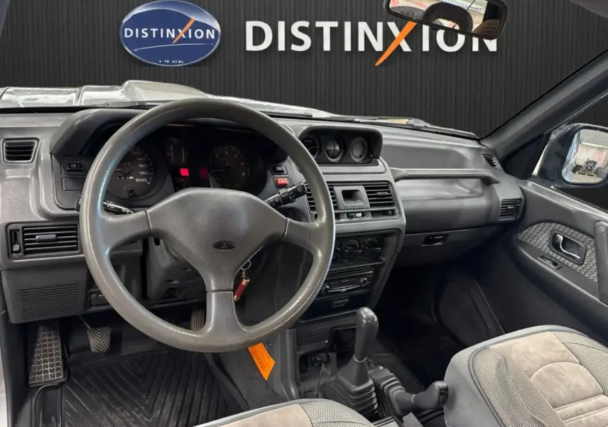 Intérieur gris du Mitsubishi Pajero Court 2.8 TD 1997, vue du poste de conduite avec volant et levier de vitesses manuel.