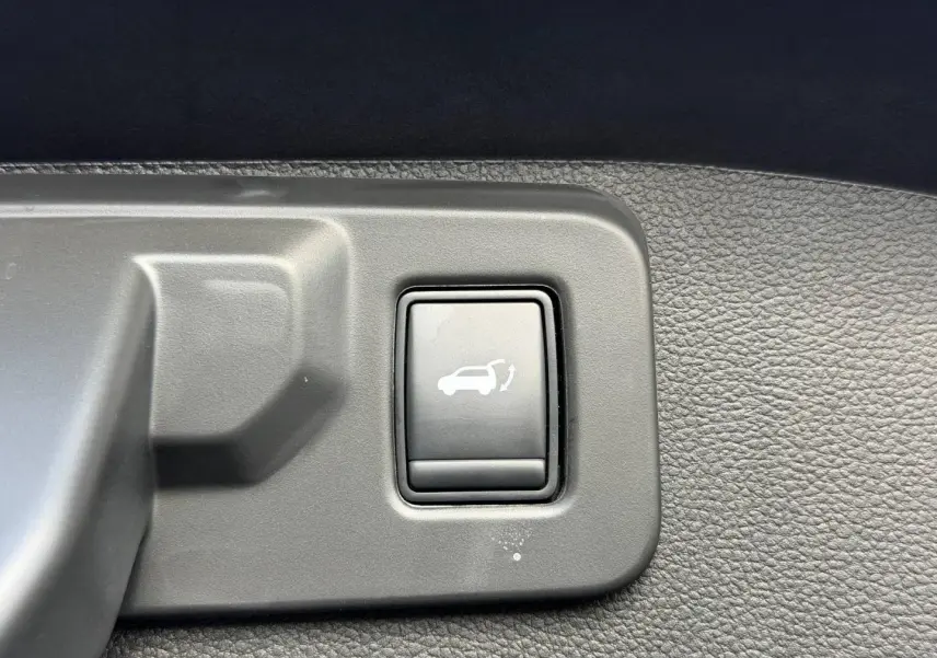 Bouton d'ouverture électrique du coffre sur panneau intérieur en plastique gris d'un Renault Austral noir étoilé.