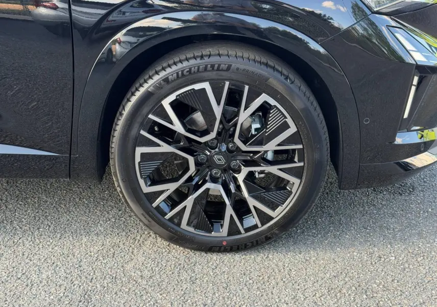 Gros plan sur la roue avant gauche noire étoilé métallisé du Renault Austral 1.2 E-Tech avec jante alu au design géométrique.