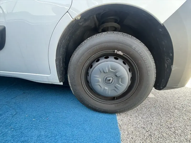 Gros plan sur la roue avant gauche blanche du Renault Master 2021 avec enjoliveur gris et pneu noir sur sol bleu et gris.