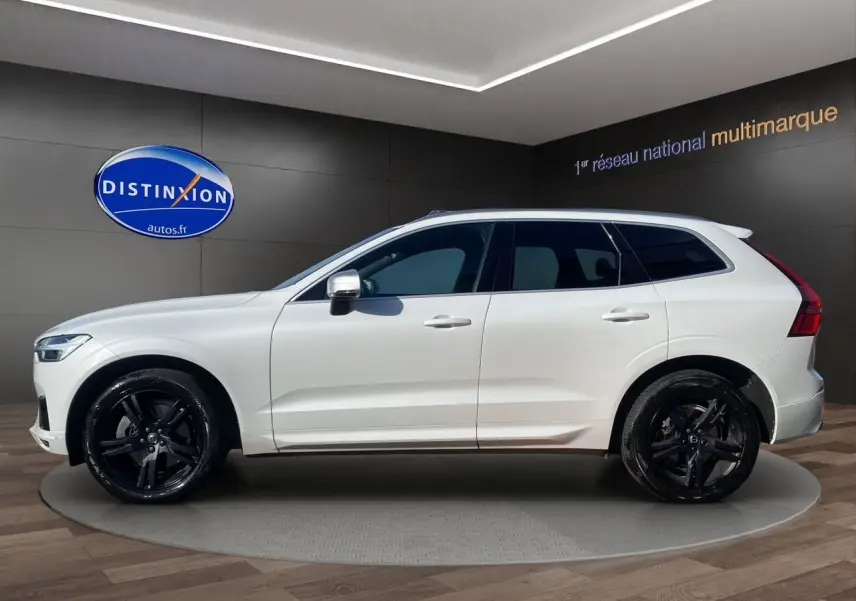Profil droit d'un Volvo XC60 blanc 2019 avec jantes noires et rétroviseurs chromés en showroom.