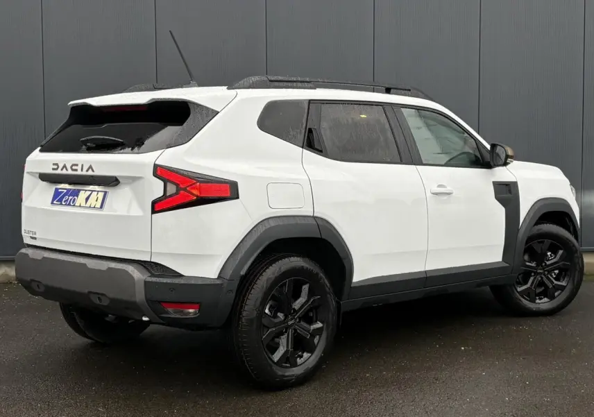 Vue 3/4 arrière droite du Dacia Duster blanc Glacier avec jantes noires et coques de rétroviseur brun cuivré.