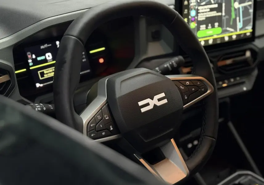 Vue rapprochée du volant multifonctions noir avec logo DACIA et tableau de bord digital du Dacia Duster 2026.