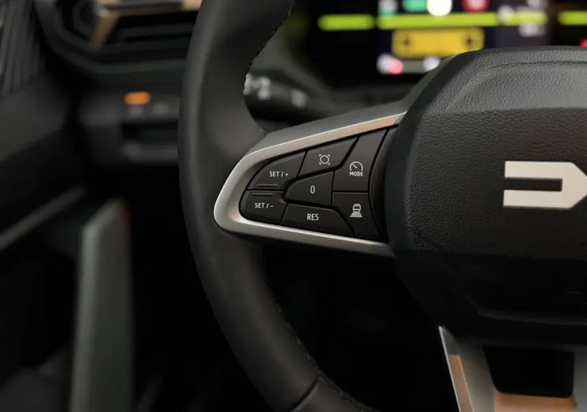 Gros plan sur les commandes au volant noir du Dacia Duster 2026, avec finition argentée et logo partiel visible.