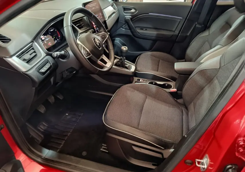 Intérieur avant droit du Renault Captur rouge 2024, volant multifonctions, sièges tissu gris et levier de vitesses manuel visible.