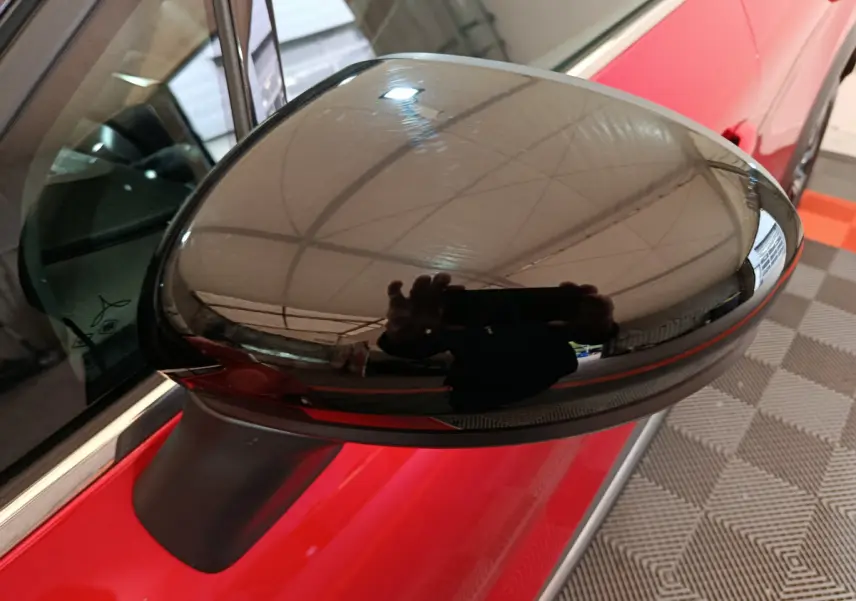 Rétroviseur noir côté gauche du Renault Captur rouge 2024 techno TCe 90, vue rapprochée sur fond intérieur.