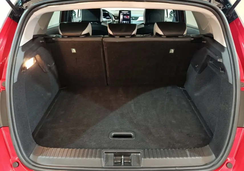 Coffre ouvert vu de l'arrière d'un Renault Captur rouge 2024, banquette arrière et écran tactile visibles à l'avant.