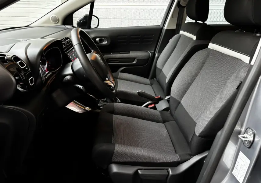 Intérieur côté conducteur du Citroën C3 Aircross gris clair 2024, sièges tissu noir et gris avec tableau de bord moderne.