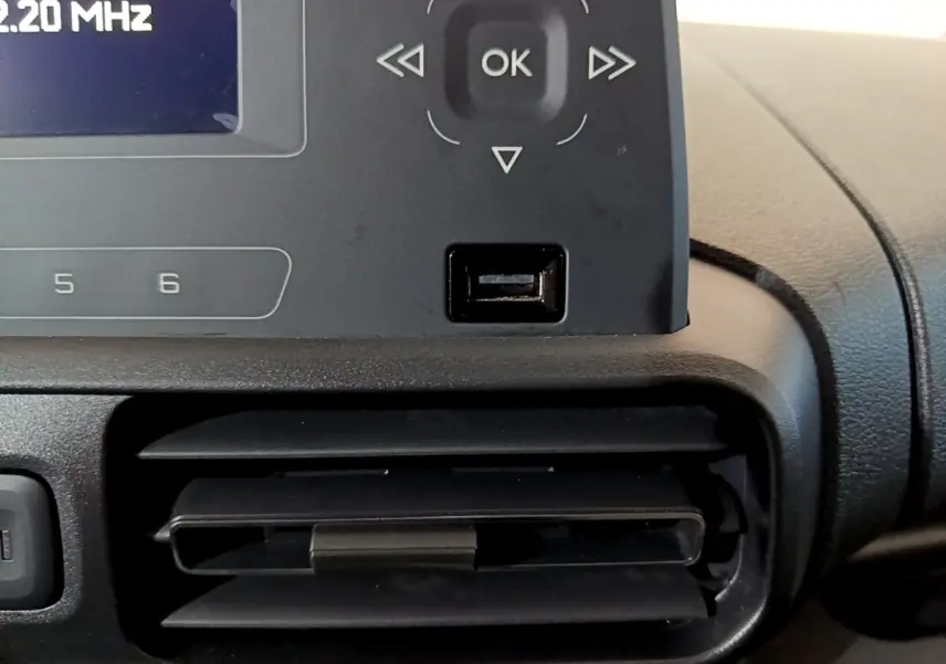 Gros plan sur la console centrale noire du Citroën Berlingo blanc, montrant l'écran radio et une prise USB sous les commandes.