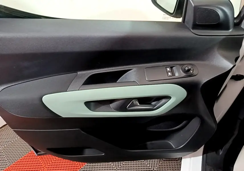 Vue intérieure du panneau de porte avant gauche du Citroën Berlingo blanc, avec poignée et commandes de vitres.