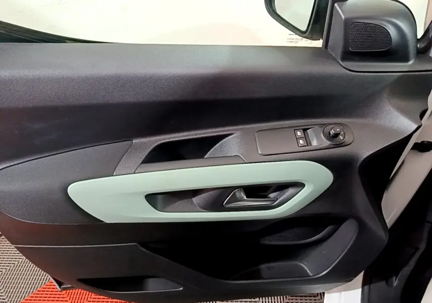Vue intérieure du panneau de porte avant gauche du Citroën Berlingo blanc, avec poignée argentée et commandes électriques.