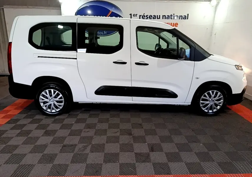 Vue de profil côté gauche d'un Citroën Berlingo XL blanc avec protections noires et jantes alliage en intérieur fermé.