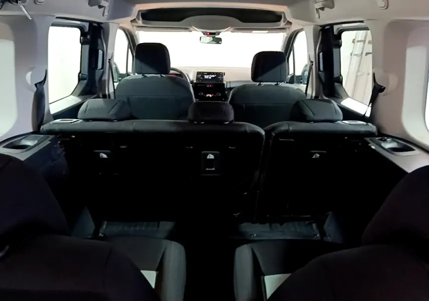 Vue intérieure arrière du Citroën Berlingo XL blanc, montrant les sièges noirs et le tableau de bord à l'avant.