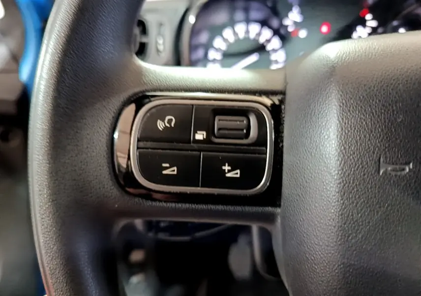 Gros plan sur les commandes au volant noir de la Citroën C3 BlueHDi 2017 avec tableau de bord flou en arrière-plan.