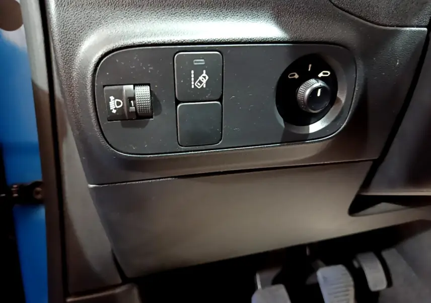 Gros plan sur les commandes côté gauche du tableau de bord d'une Citroën C3 bleue, avec réglage des phares et des rétroviseurs.
