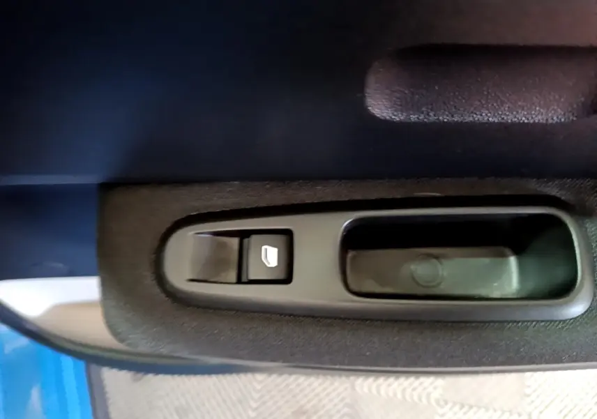 Gros plan sur la commande de lève-vitre côté conducteur d'une Citroën C3 bleu 2017, intérieur tissu noir.