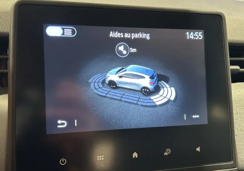 Écran tactile intérieur montrant l'aide au parking avec une voiture grise en vue 3/4 arrière sur fond noir.