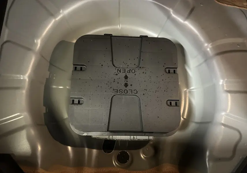 Coffre à roue de secours ouvert vu de dessus sur Renault Clio V noire, montrant le compartiment métallique intérieur.