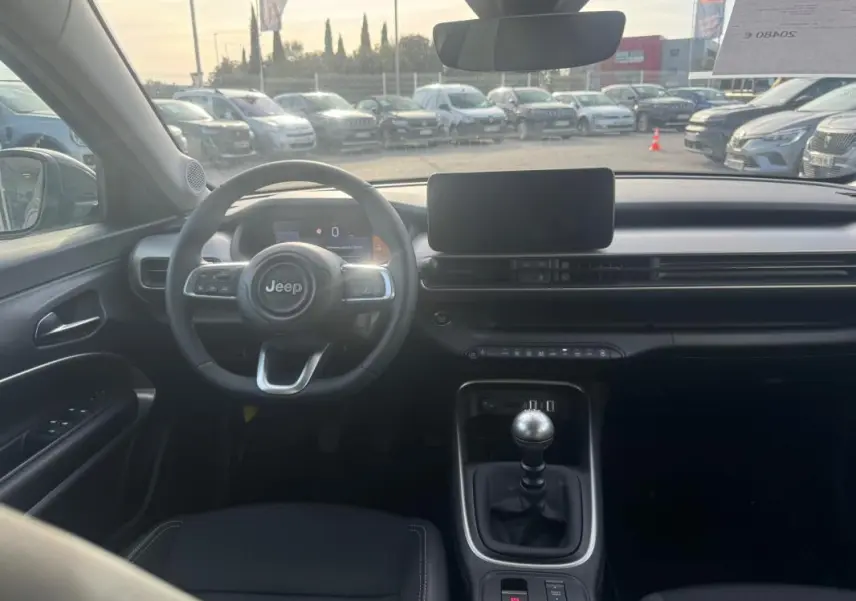 Vue intérieure frontale du Jeep Avenger gris 2025, avec volant multifonction, écran central et levier de vitesse manuel.