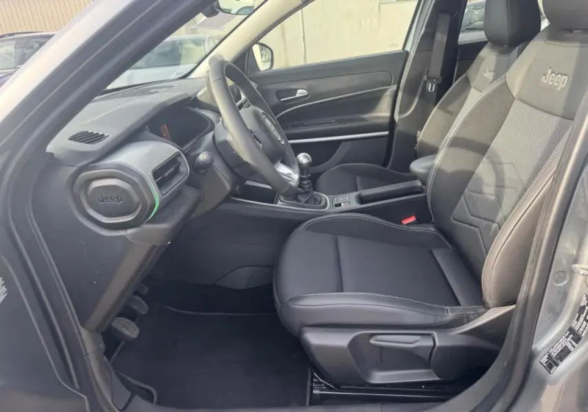 Vue intérieure côté conducteur du Jeep Avenger gris 2025, mettant en valeur les sièges noirs avec logo Jeep et la boîte manuelle.