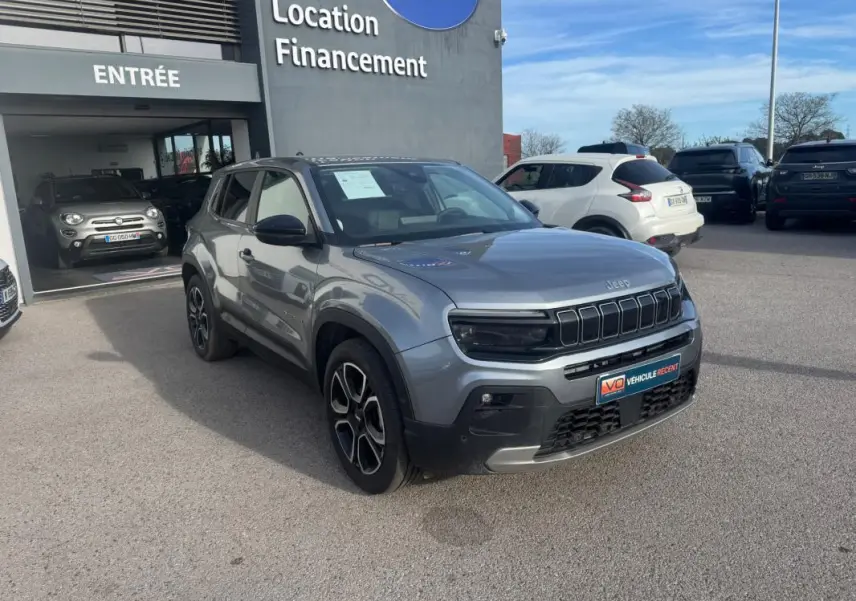 Jeep Avenger gris 3/4 avant droit, SUV compact avec calandre noire distinctive, stationné devant un concessionnaire.