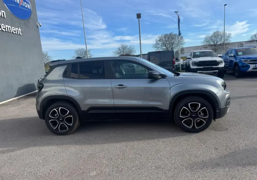 Vue de profil côté gauche d'un Jeep Avenger gris 2025 avec jantes distinctives et lignes noires sur les bas de caisse.