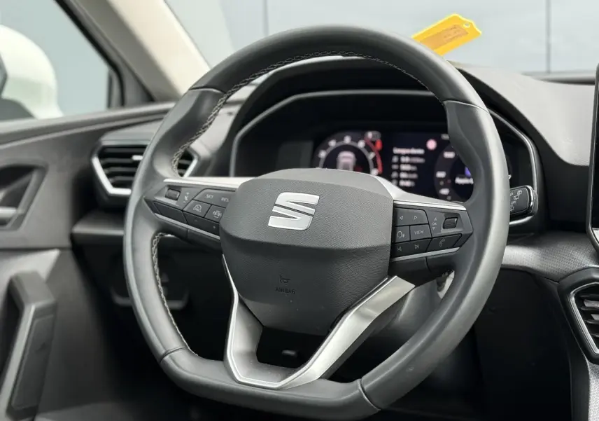 Vue rapprochée du volant cuir multifonction noir avec logo SEAT, tableau de bord numérique en arrière-plan.