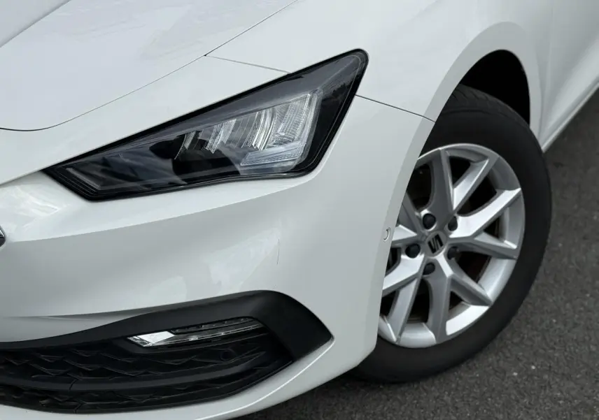 Gros plan sur l'avant droit blanc d'une SEAT LEON 2025, mettant en valeur le projecteur LED et la jante alliage 16 pouces.