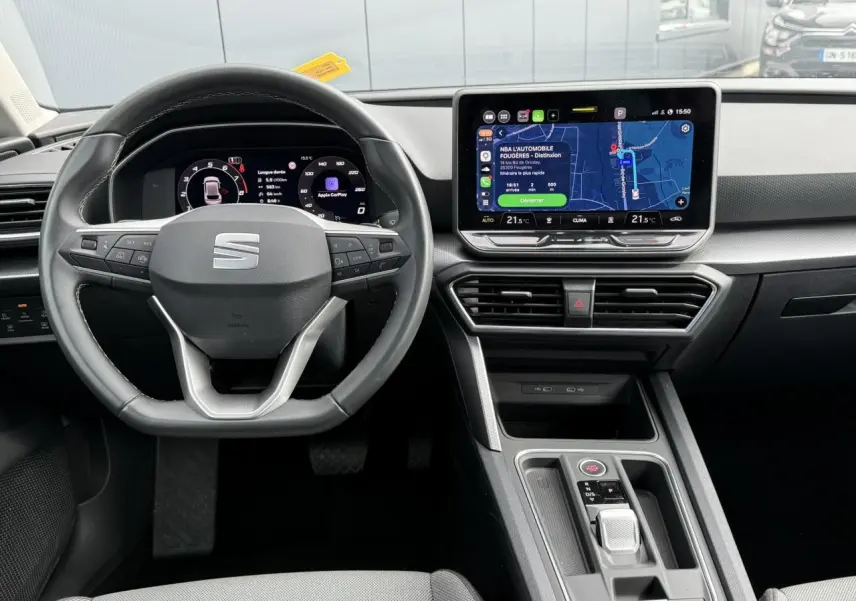 Vue intérieure frontale du poste de conduite de la SEAT LEON 2025 avec volant multifonction et écran tactile central allumé.