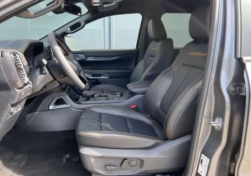 Vue intérieure côté conducteur du Ford Ranger Wildtrak Plus 2025, sièges cuir noirs avec surpiqûres orange et volant multifonctions.