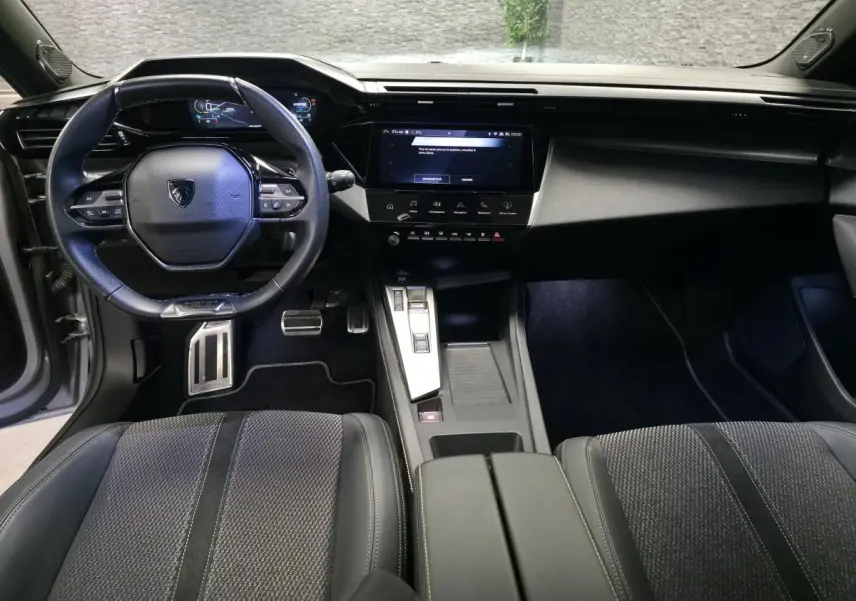Vue intérieure avant de la Peugeot 308 GT 2024, tableau de bord noir avec écran tactile central et volant cuir.