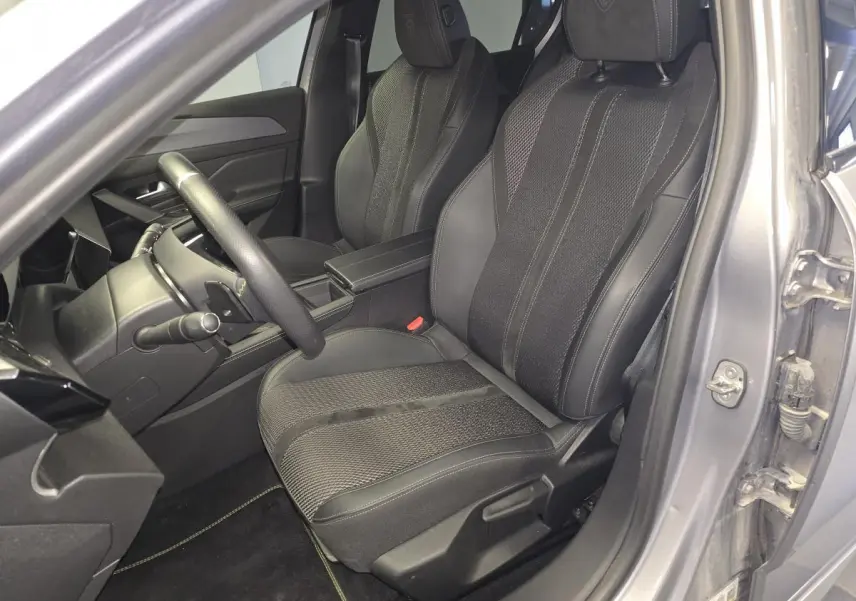 Vue intérieure côté conducteur de la Peugeot 308 gris 2024, sièges sport en tissu et cuir avec logo Peugeot brodé.