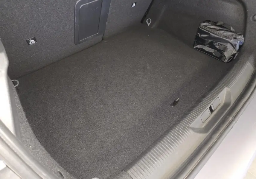 Vue intérieure du coffre gris du Peugeot 308 1.6 PHEV 2024 avec sac de rangement noir sur le côté droit.