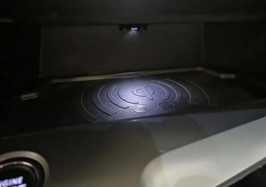 Gros plan sur le chargeur à induction noir dans l'habitacle de la Peugeot 308 gris 2024, éclairé par une LED.