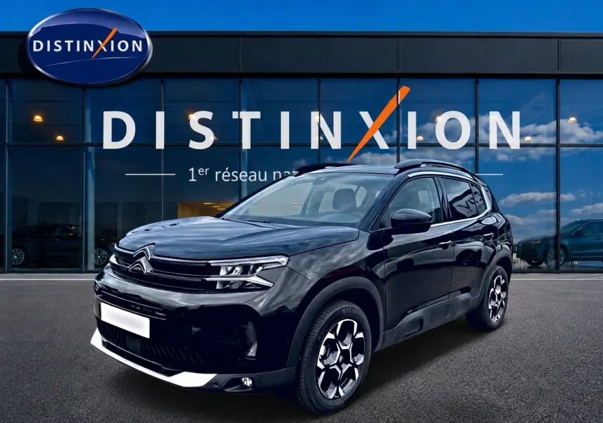 Citroën C5 Aircross noir vue 3/4 avant droit, avec jantes alu et barres de toit visibles devant une vitrine Distinxion.