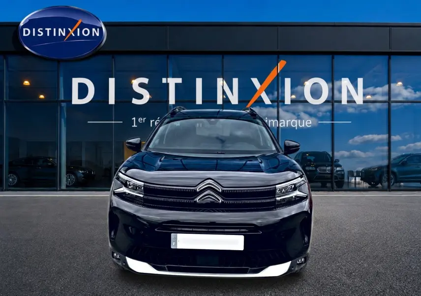 Vue frontale d'un Citroën C5 Aircross noir 2025 avec calandre distinctive et barres de toit visibles devant une vitrine.