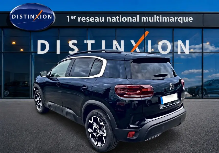 Citroën C5 Aircross noir vue 3/4 arrière droit, avec jantes alu et barres de toit devant showroom Distinxion.