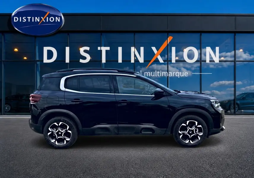 Profil côté gauche du Citroën C5 Aircross noir 2025 avec jantes alu et barres de toit visibles devant une vitrine Distinxion.