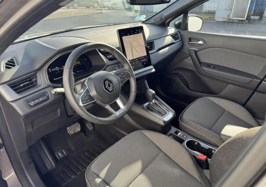 Vue intérieure côté conducteur du Renault Captur II gris Cassiopée, volant multifonction et écran tactile vertical avec navigation affichée.