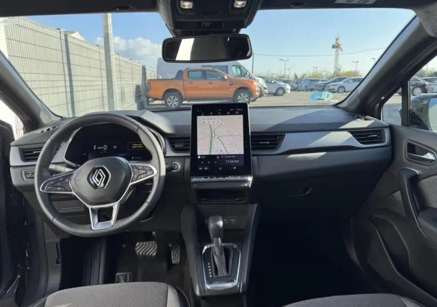 Vue intérieure avant du Renault Captur gris Cassiopée, avec tableau de bord numérique et écran tactile central affichant la navigation.