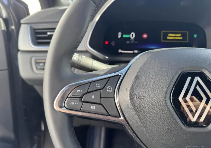 Gros plan sur le volant côté gauche du Renault Captur gris Cassiopée 2025 avec commandes intégrées et tableau de bord numérique.