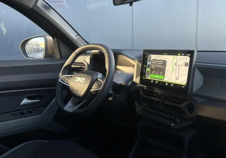 Vue intérieure côté conducteur du Dacia Duster 2025 avec volant multifonction, écran tactile GPS et détails brun cuivré.