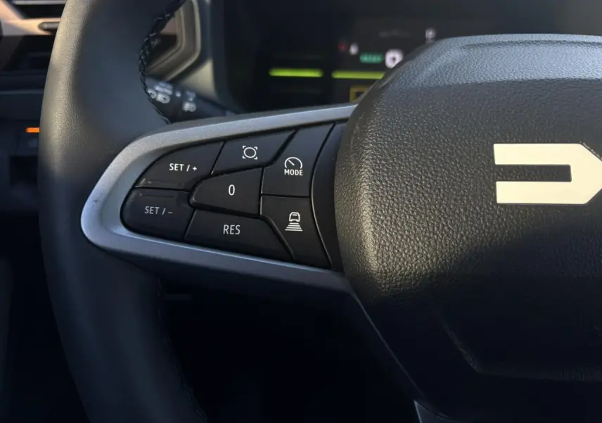 Gros plan sur le côté gauche du volant noir du Dacia Duster 2025, avec commandes de régulateur de vitesse et finition argentée.