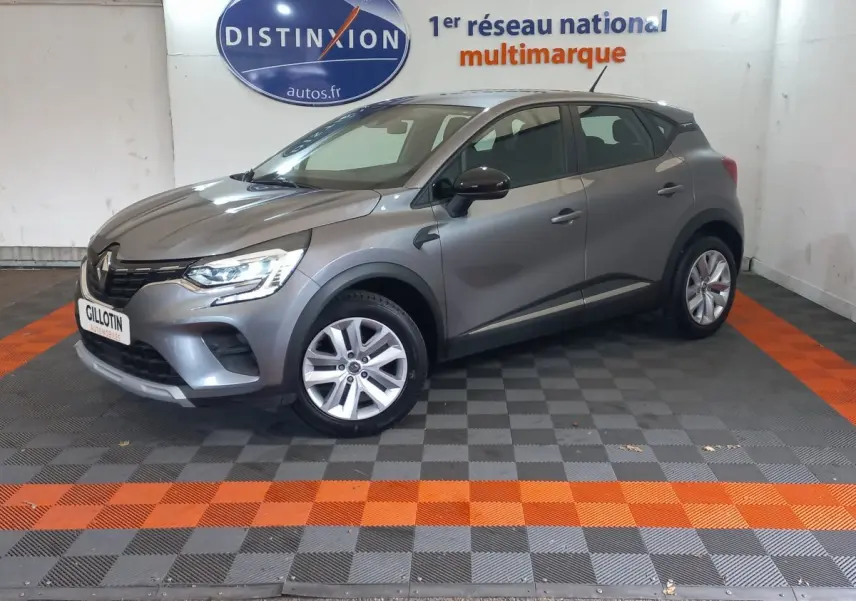 Renault Captur Business TCe 100 gris clair vu de profil côté gauche dans un showroom avec sol gris et orange.