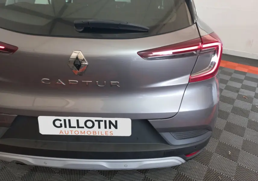 Vue arrière droite d'un Renault Captur gris clair avec feux LED et logo visible sur un sol à motifs.