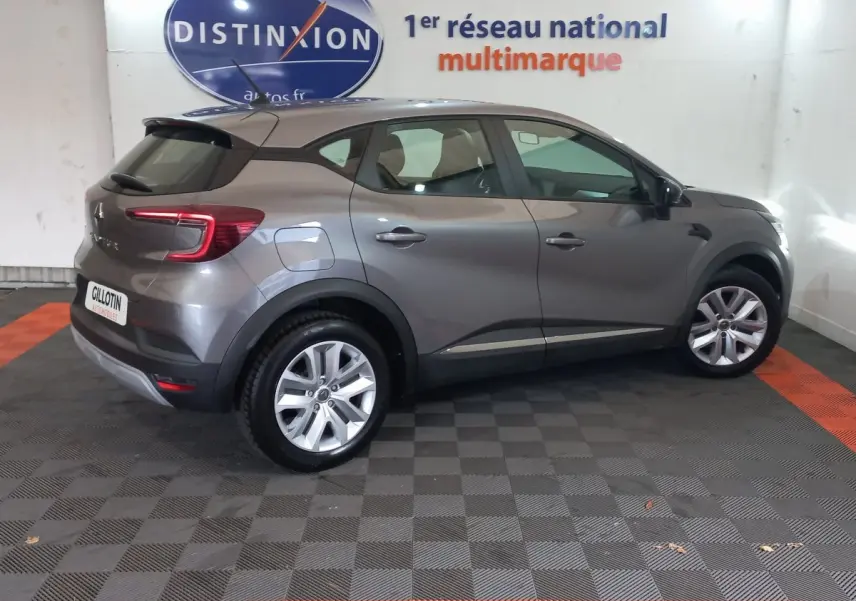 Renault Captur Business gris clair vu de profil côté droit, stationné en intérieur avec logo Distinxion en arrière-plan.